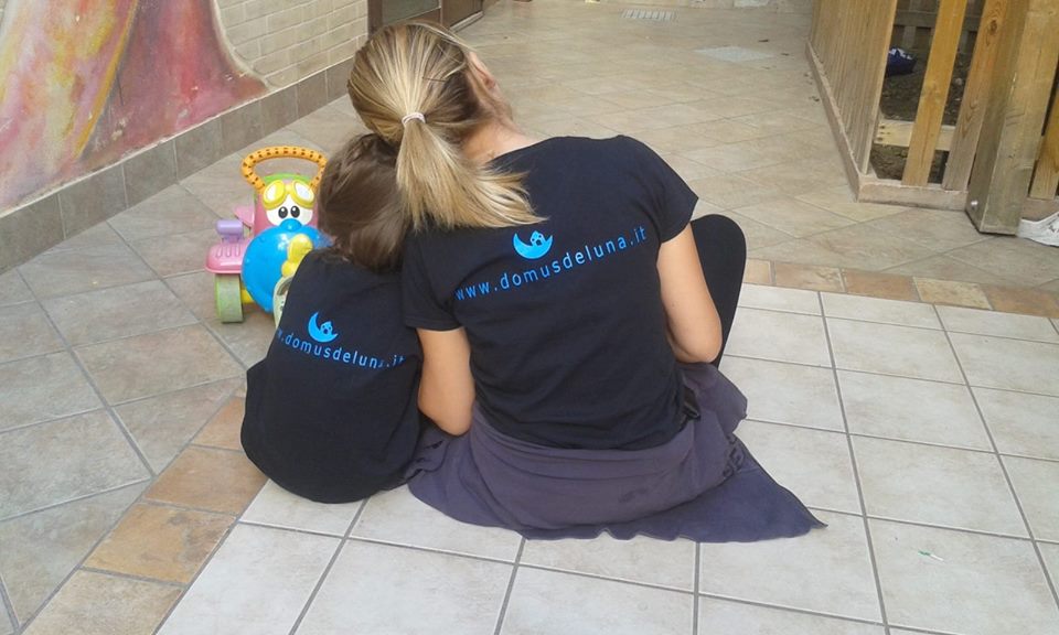 Operatrice e bambino seduti di spalle con la maglietta di Domus de Luna