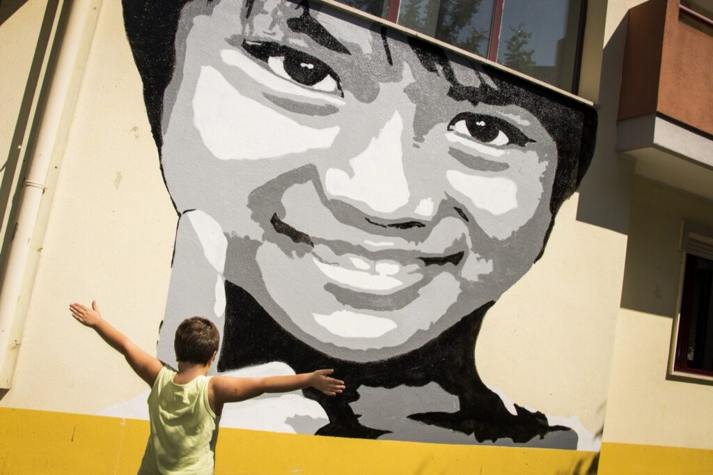 Murale con il volto sorridente di una bambina e un bambino a braccia aperte