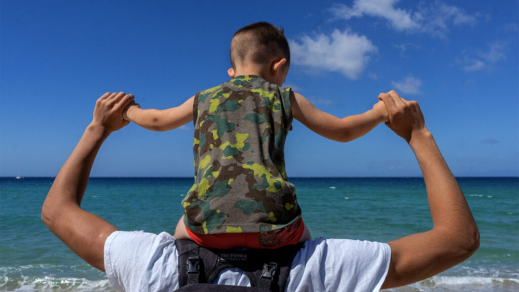 Papà con il bambino sulle spalle davanti al mare